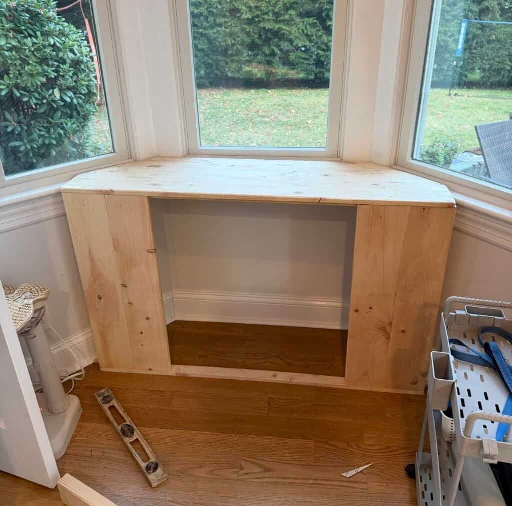 Raw pine 1x4 cabinet frame built into a bay window nook